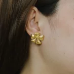 Female model wearing 18K gold-plated flower stud earrings to showcase fit for Established brands