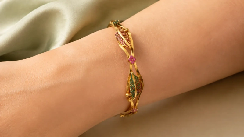 Female wrist wearing a gold brass bangle with green and pink enamel leaves