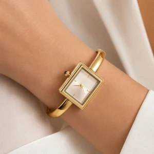 Close-up of a gold-tone stainless steel square watch bangle bracelet worn on a partial wrist, highlighting the minimalist square dial and polished bangle design.