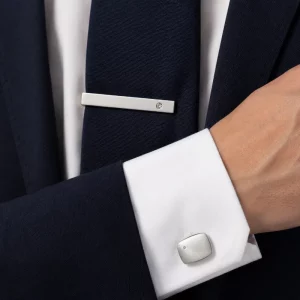 Silver cufflinks and tie clip set displayed with a navy suit and white shirt.