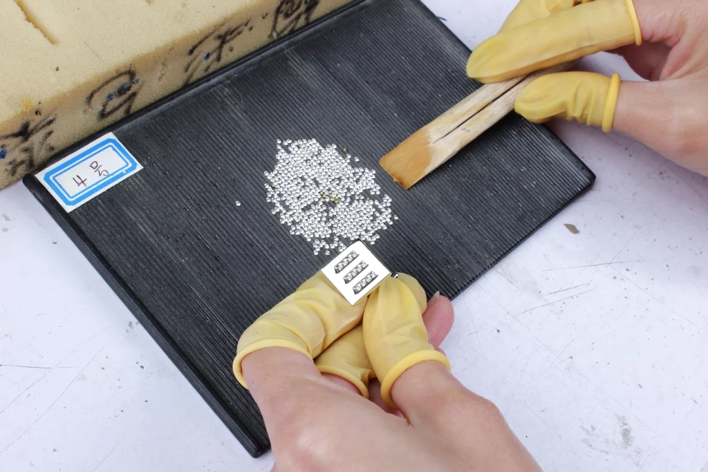 Worker handling small stones and checking a stone-set jewelry component during production