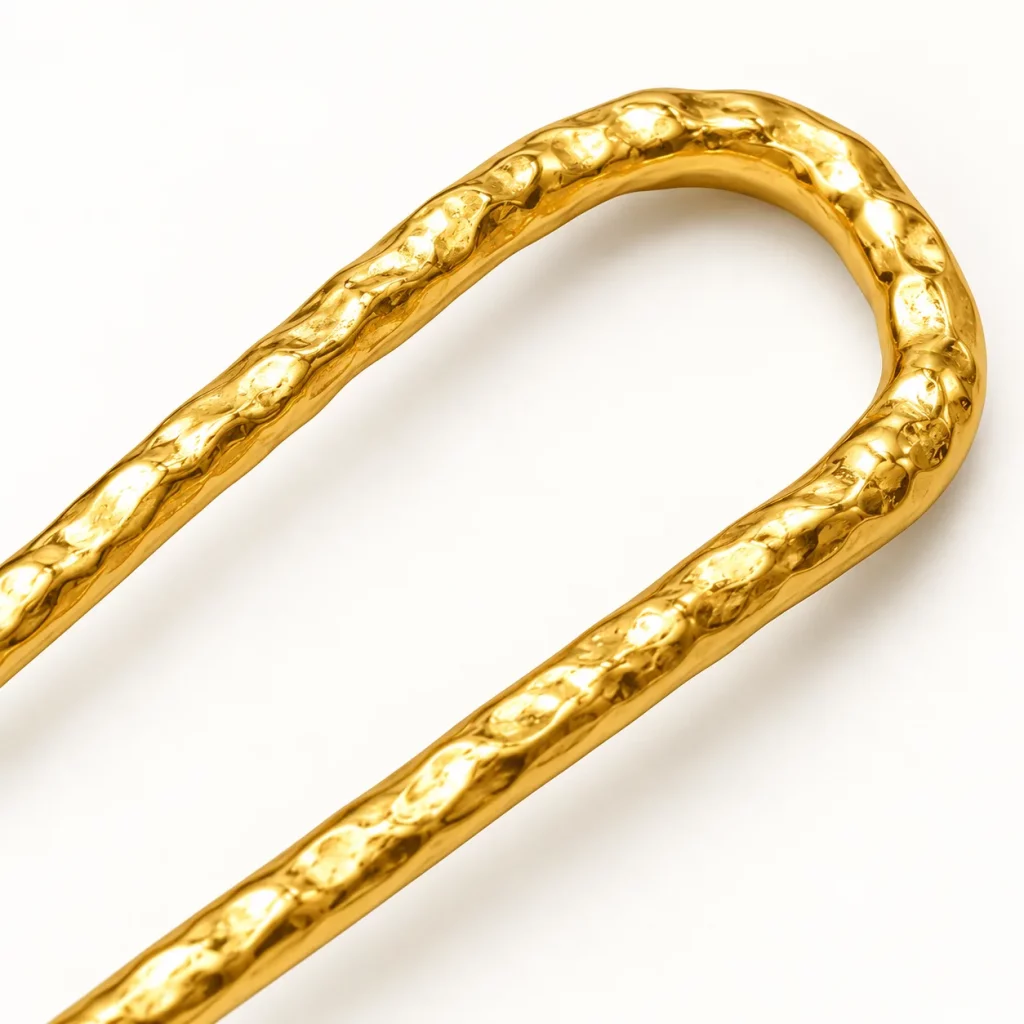 Close-up of the hammered texture and polished 18K gold-plated finish on a U-shaped two-prong hair fork.