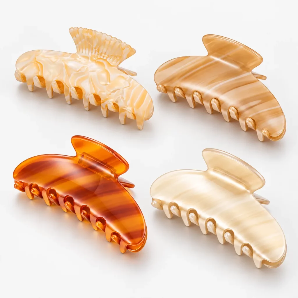 Four cellulose acetate hair claw clips in cream marble, honey stripe, amber orange and ivory finishes.
