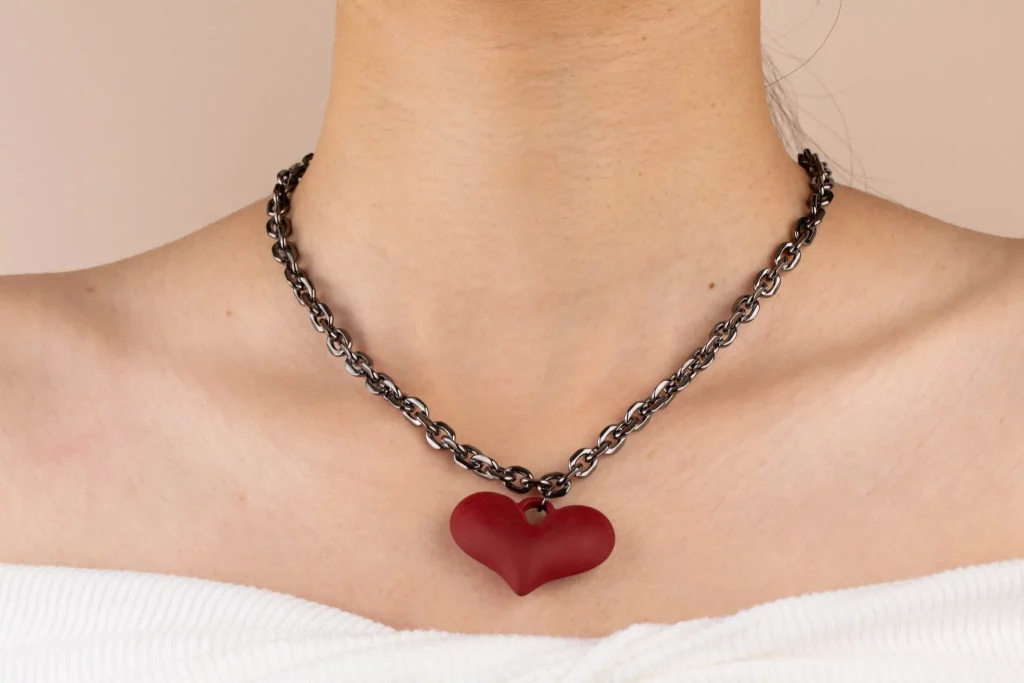 Model wearing a red heart pendant necklace with a dark metal chain and white off-shoulder top