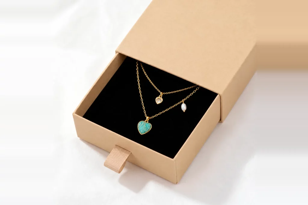 Layered gold-tone heart necklaces displayed in a beige jewelry gift box with black velvet interior