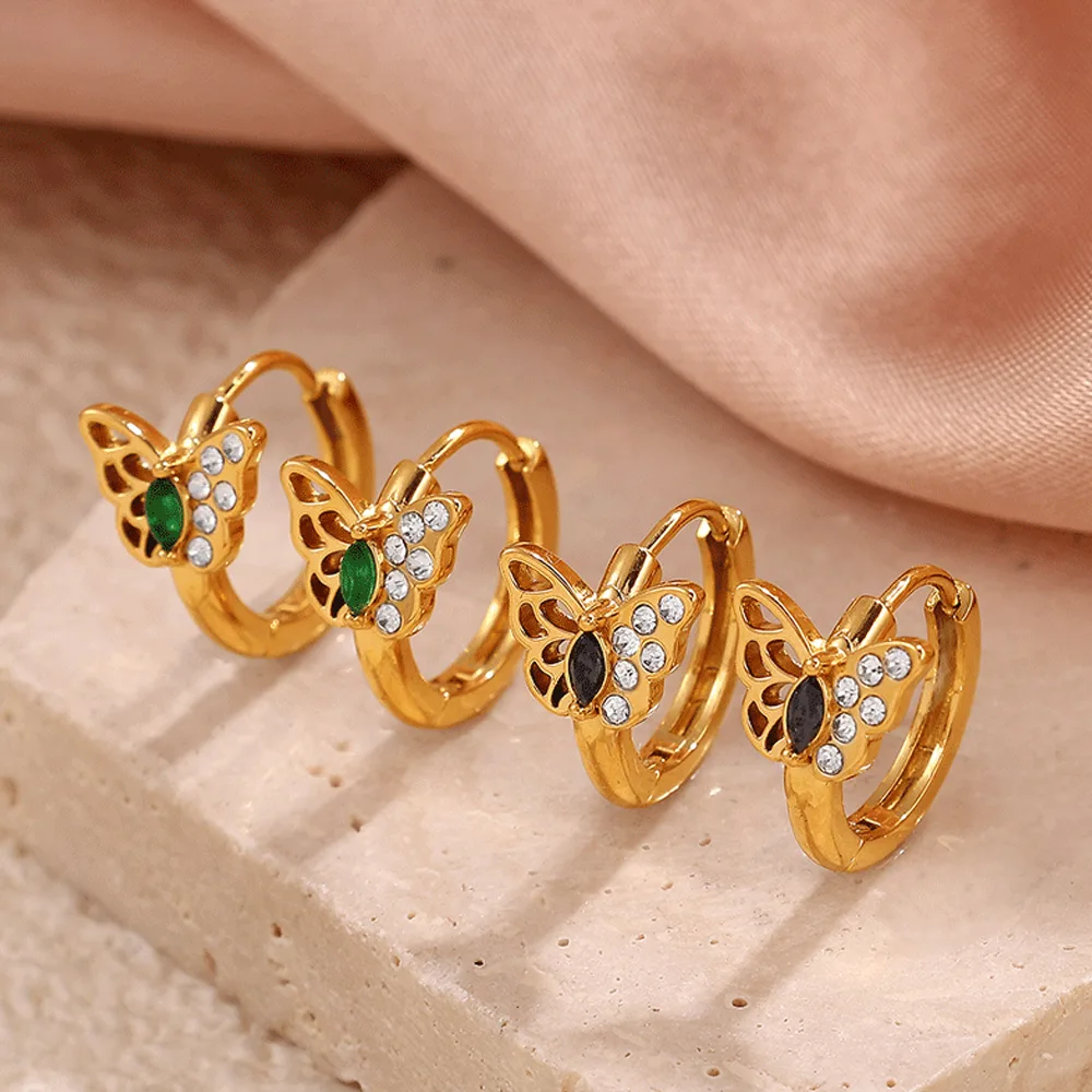Butterfly stainless steel rhinestone huggie earrings in gold plated finish displayed on a stone pedestal