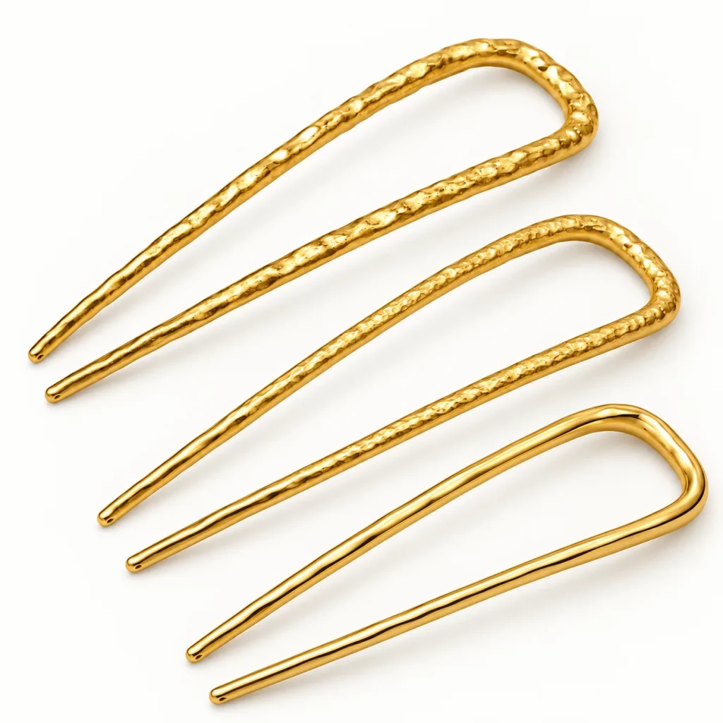 Three gold-tone U-shaped two-prong hair forks showing different hammered textures and profile proportions for custom development.