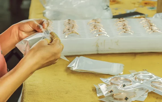 Close-up of a worker carefully packaging gold-plated clover bracelets into individual protective poly bags at a jewelry manufacturing factory.